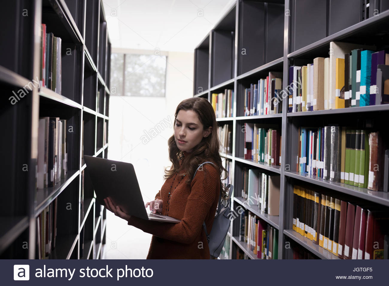 Female college student with laptop researching among bookshelves in library Stock Photo Alamy