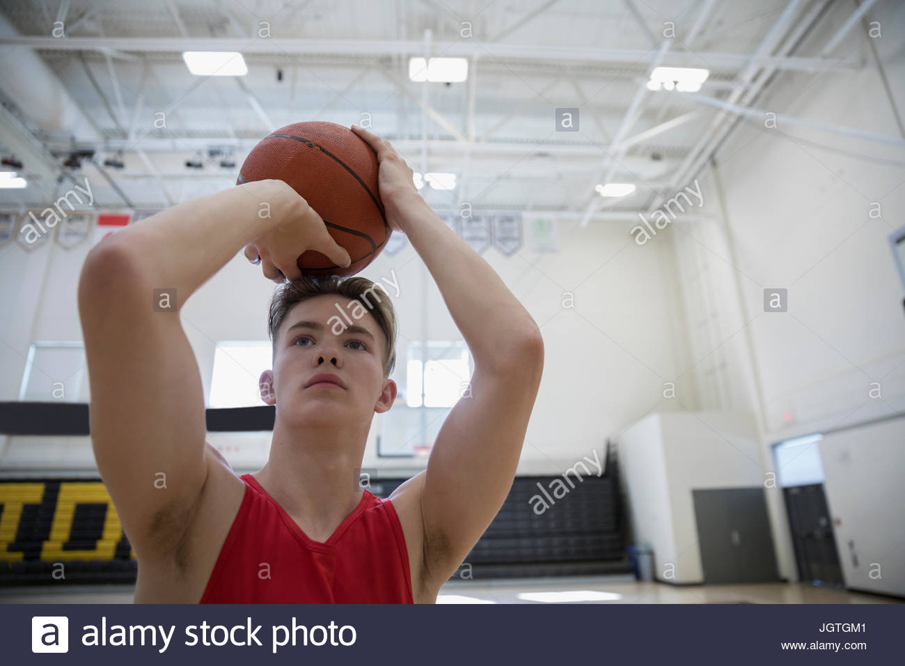 Focused male college basketball player shooting basketball in gymnasium Stock Photo