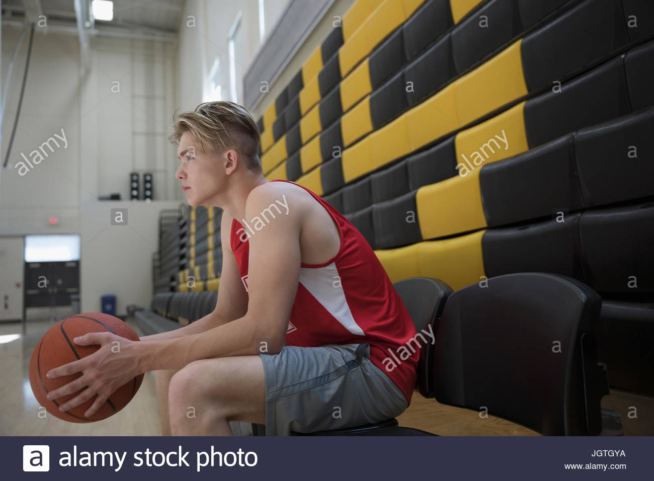 Serious male college basketball player sitting on bench in gymnasium Stock Photo