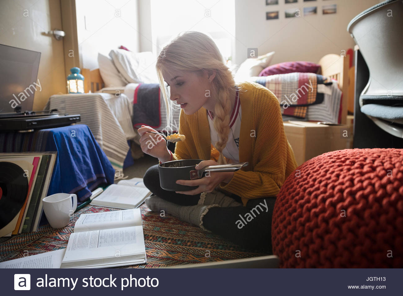 Female college student eating and studying on floor in dorm room Stock Photo