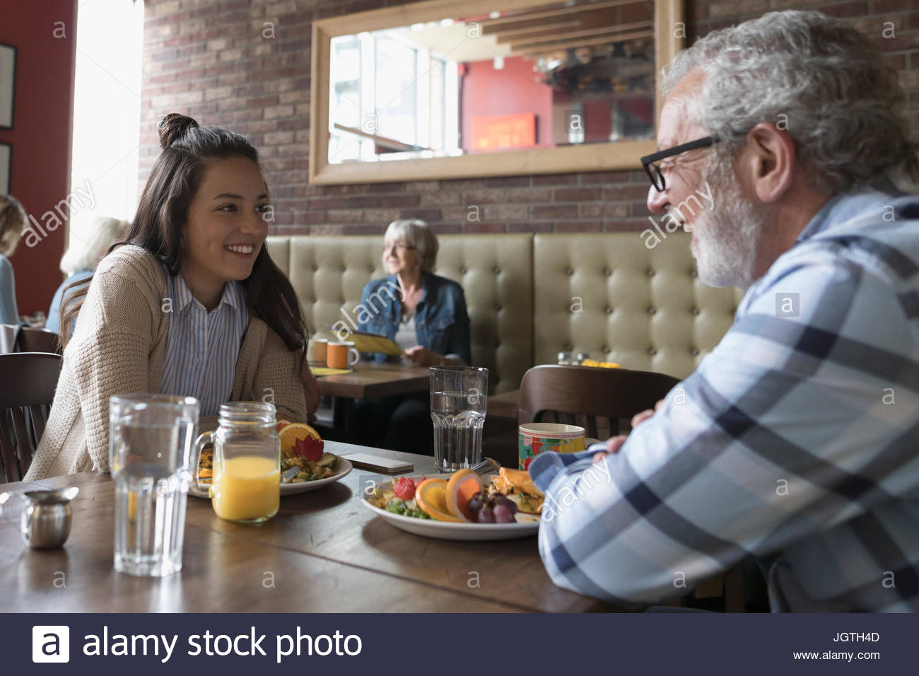 Grandfather and teenage granddaughter talking, eating brunch at diner table Stock Photo