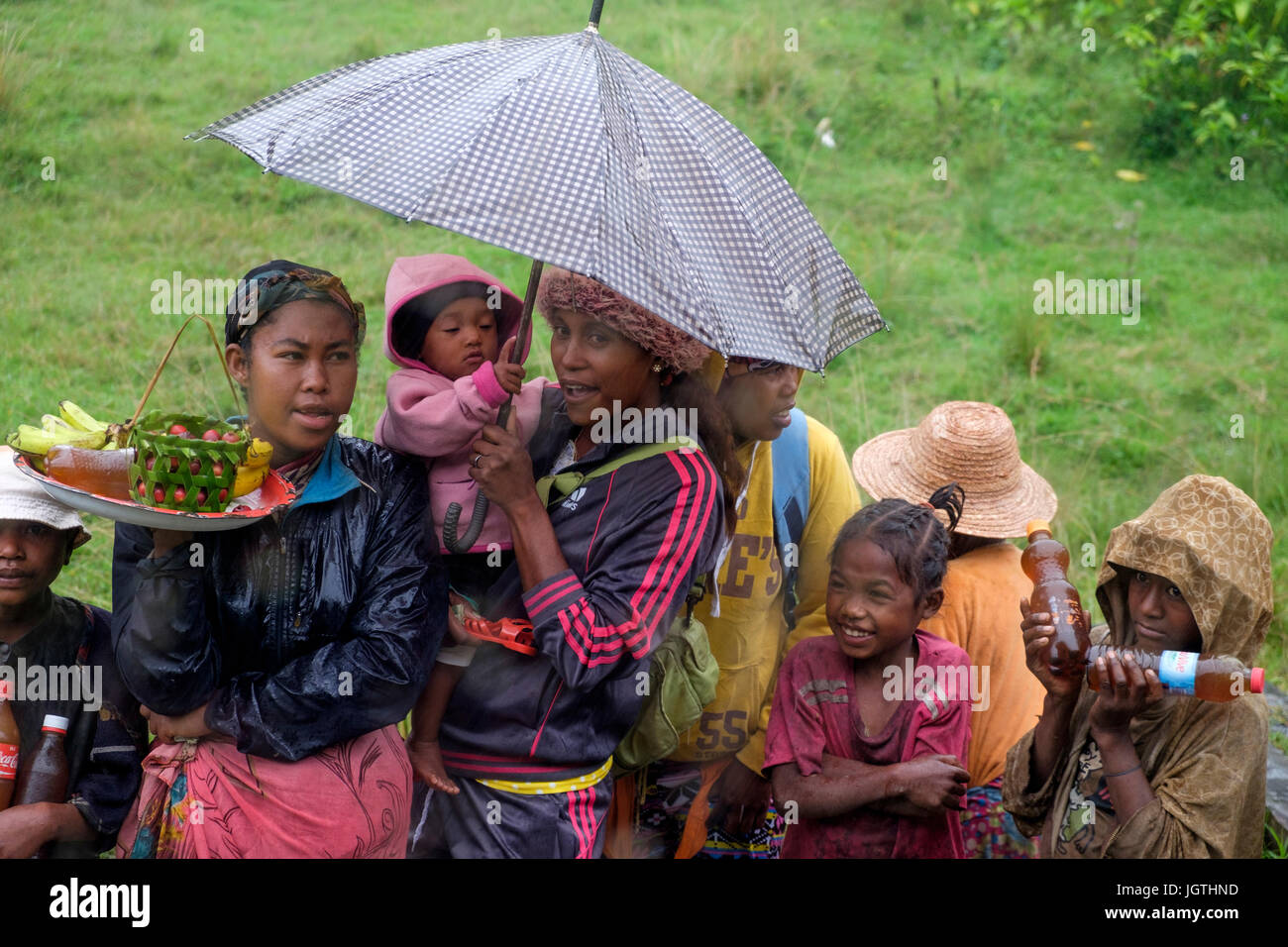 Local people brave the rain to sell fruit, drinks and honey at one of the stations along the Fianarantsoa-Côte Est railway in Madagascar Stock Photo
