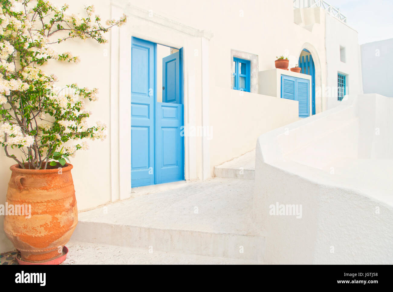 view of small street with traditional Greek white buildings with blue doors and windows and flower pot at foreground on spring day, Oia, Santorini, Gr Stock Photo