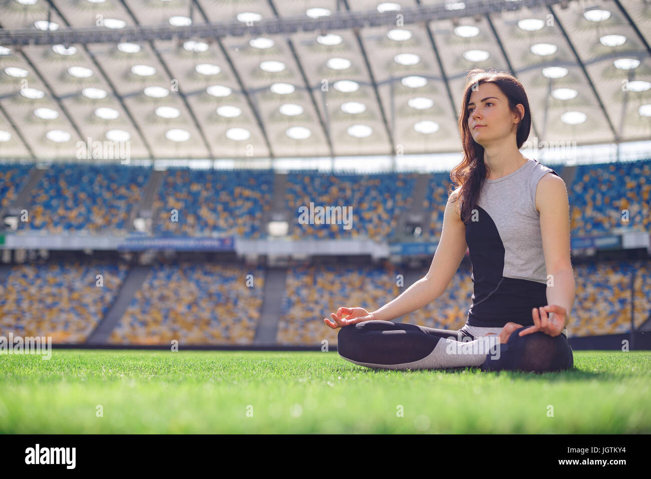 Young happy sporty girl sitting in yoga pose at the stadium. Yoga woman ...
