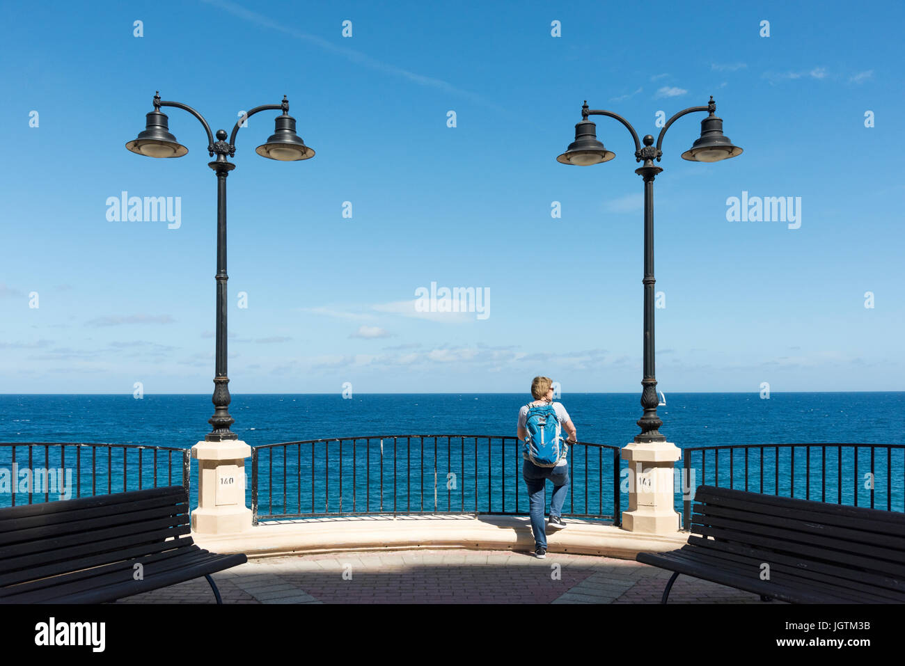 A woman looking out to sea on the promenade on the coast at Sliema Malta between two lamposts Stock Photo