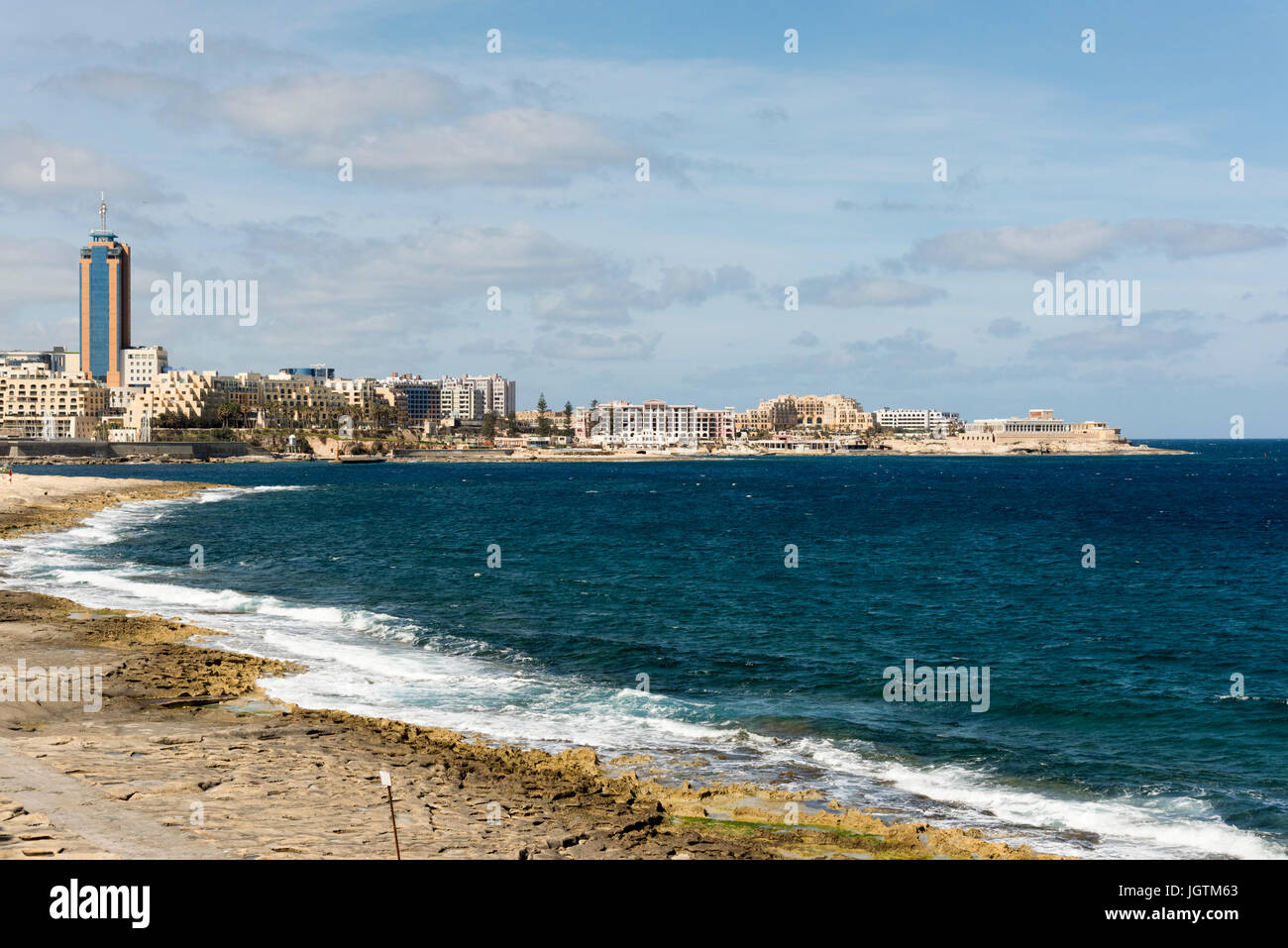 The rocky shore and sea at St Julians Bay Malta with the town of St Julians and the Pormaso tower in the background Stock Photo