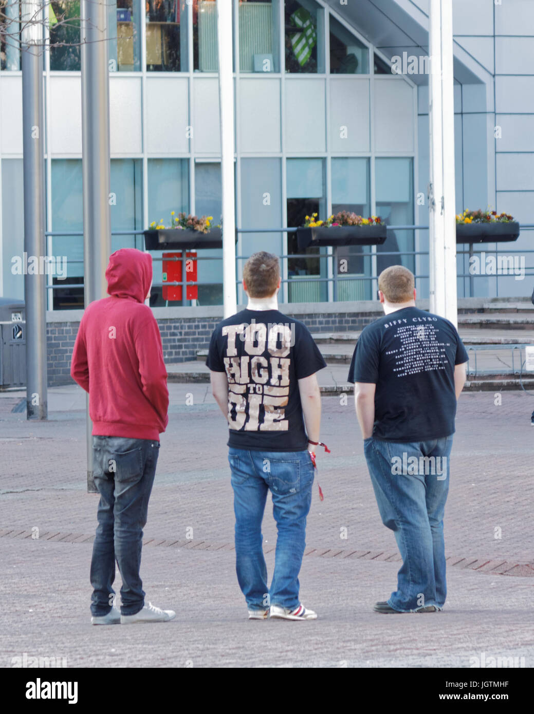 three young guys students teenagers boys viewed from behind in a cityscene setting 'too high to die tee shirt' hoody hoodie Stock Photo