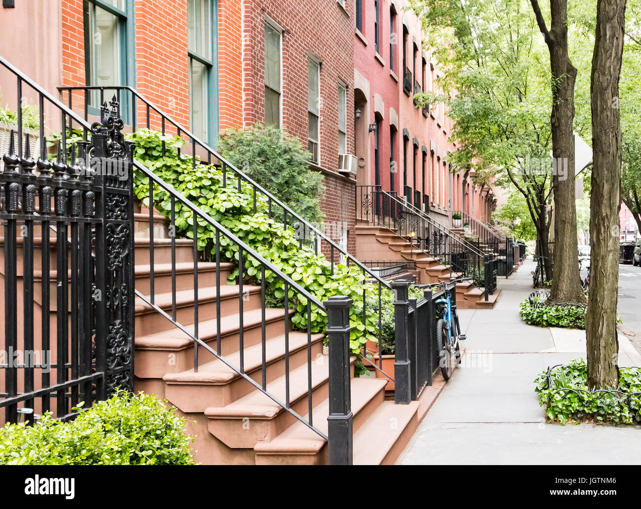 Scenic tree lined street of historic brownstone buildings in the West Village neighborhood of Manhattan in New York City, NYC USA Stock Photo