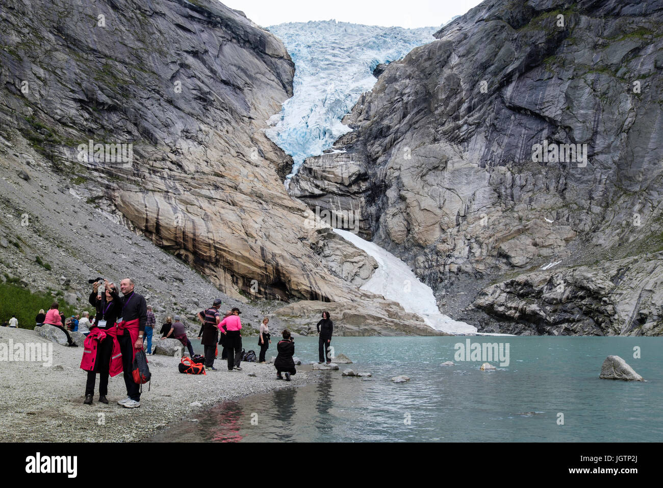 Tourists visiting Briksdalsbreen or Briksdal glacier arm of Jostedalsbreen above Briksdalsbrevatnet lake in Jostedalsbreen National Park, Norway Stock Photo