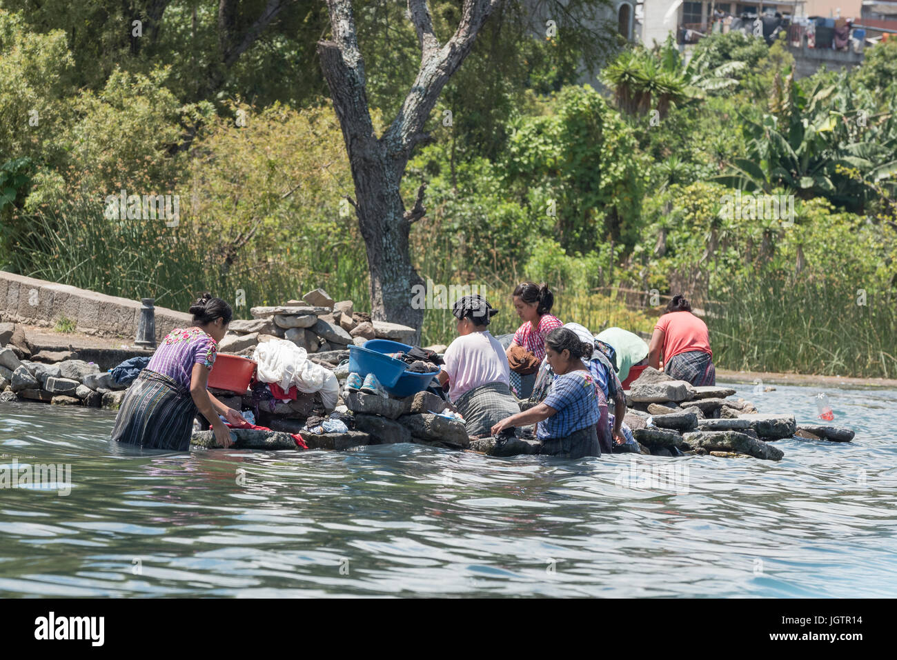 Several women of mixed ages in the typical native dress cleaning and washing clothes, Lake Atitlan,  Guatemala Stock Photo