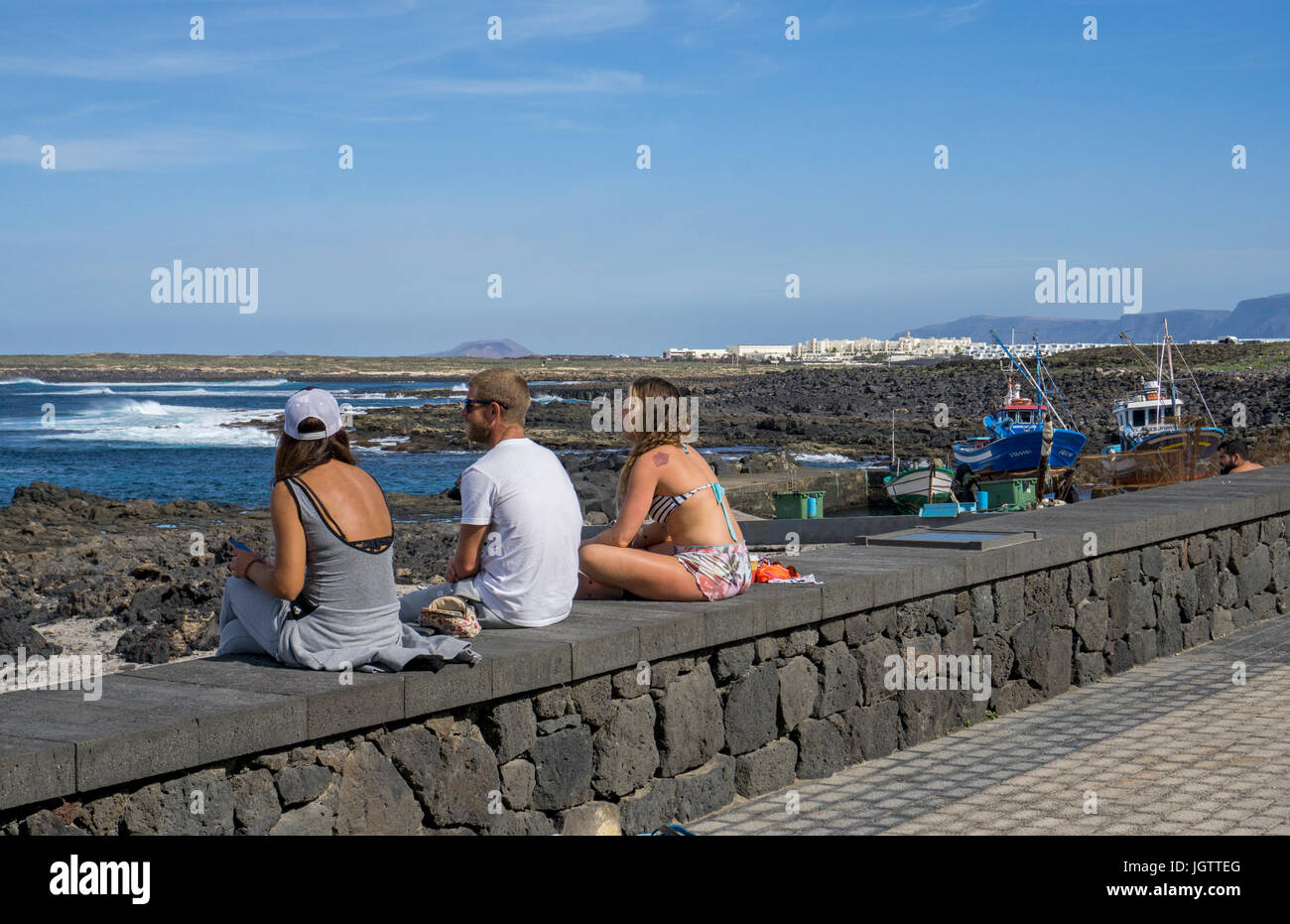 Young people sitting on harbour mural, village La Santa at north coast of Lanzarote island, Canary islands, Spain, Europe Stock Photo