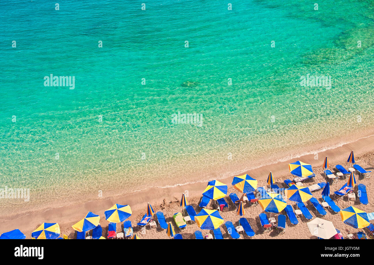 beach with colourful sunbeds and umbrellas by clear turquoise blue waters of Mediterranean sea on sunny hot summer day, Crete, Greece Stock Photo