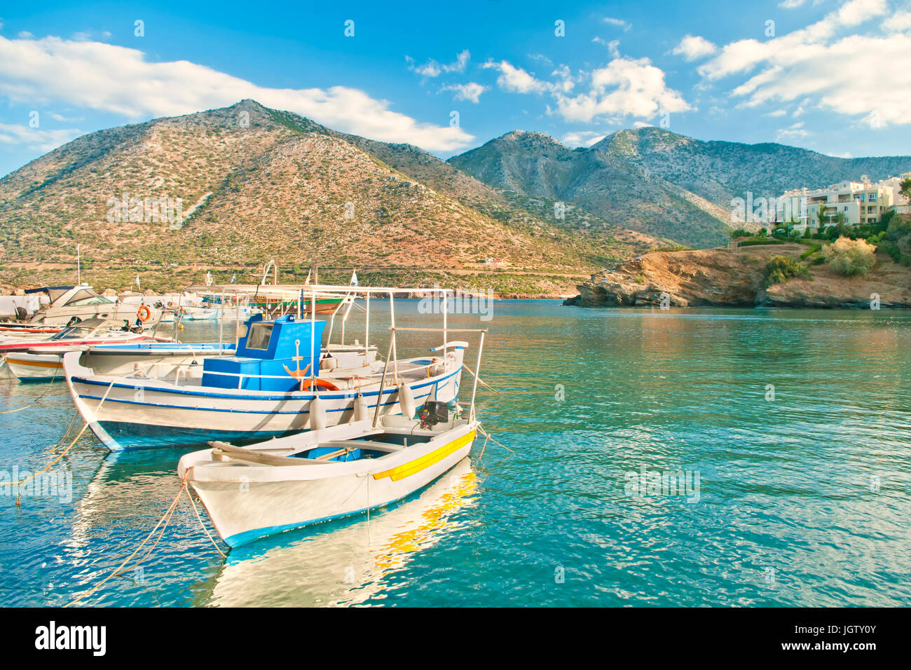 small fishing boats moored at pier in fishing village named Bali at sunset with mountains at background in Crete, Greece Stock Photo