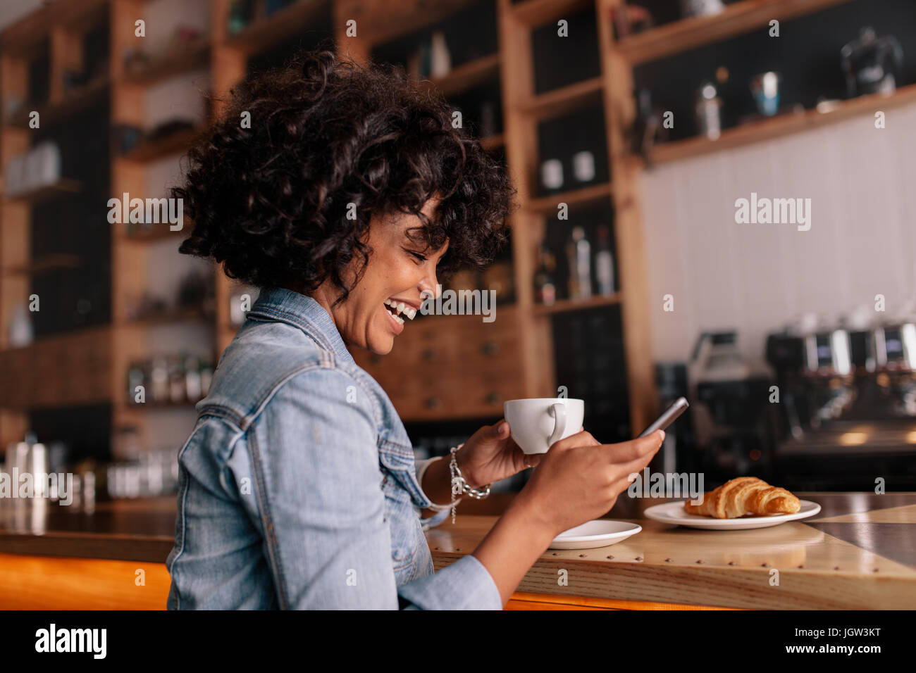 Side view shot of smiling young african woman sitting at cafe counter ...