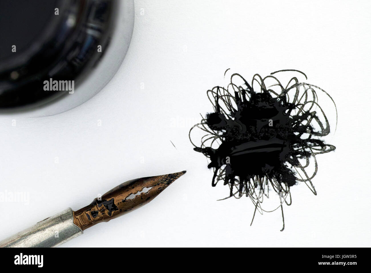 Black ink spot on white paper with pen and bottle of ink. Stock Photo