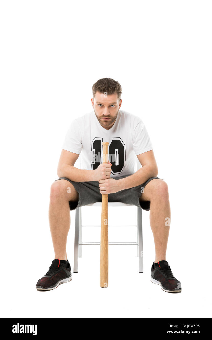 Serious Man Holding Baseball Bat While Sitting On Chair Isolated