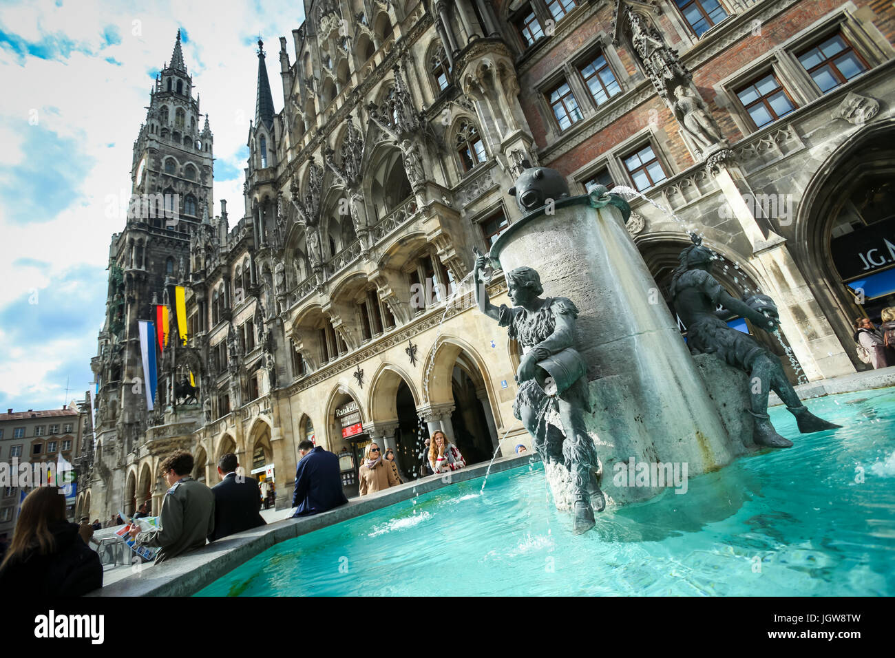 MUNICH, GERMANY - MAY 9, 2017 : People sitting on the edge of Fish Fountain with New Town Hall in the background at Marienplatz in Munich, Germany. Stock Photo