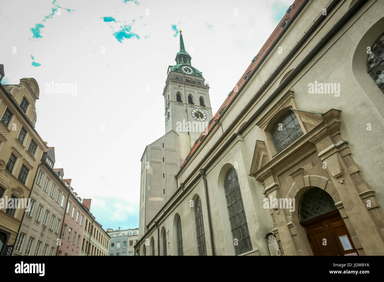 MUNICH, GERMANY - MAY 9, 2017 : A low angle view of the Saint Peters church clock tower among the city buildings in Munich, Germany. Stock Photo