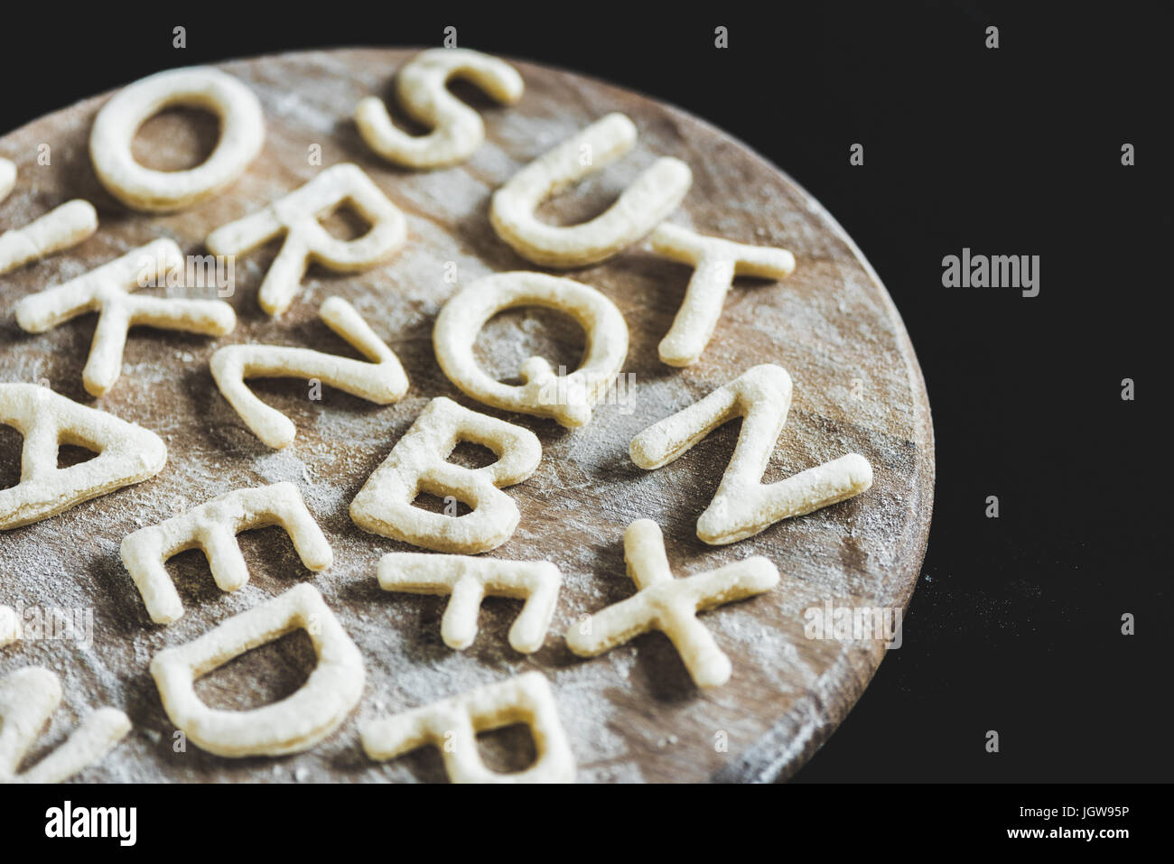 close up view of letters made from cookie dough on wooden board with flour isolated on black Stock Photo