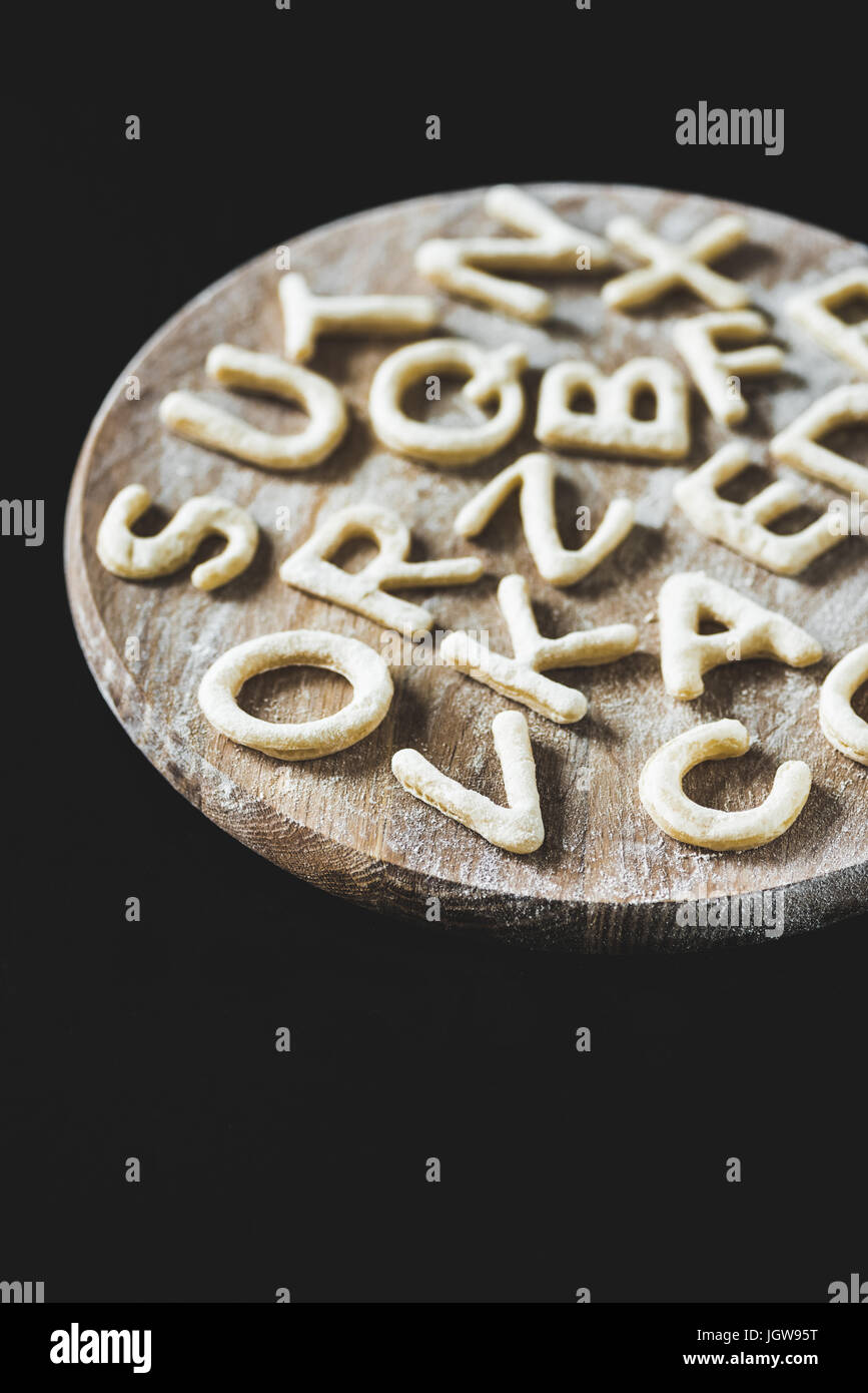 close up view of letters made from cookie dough on wooden board with flour isolated on black Stock Photo