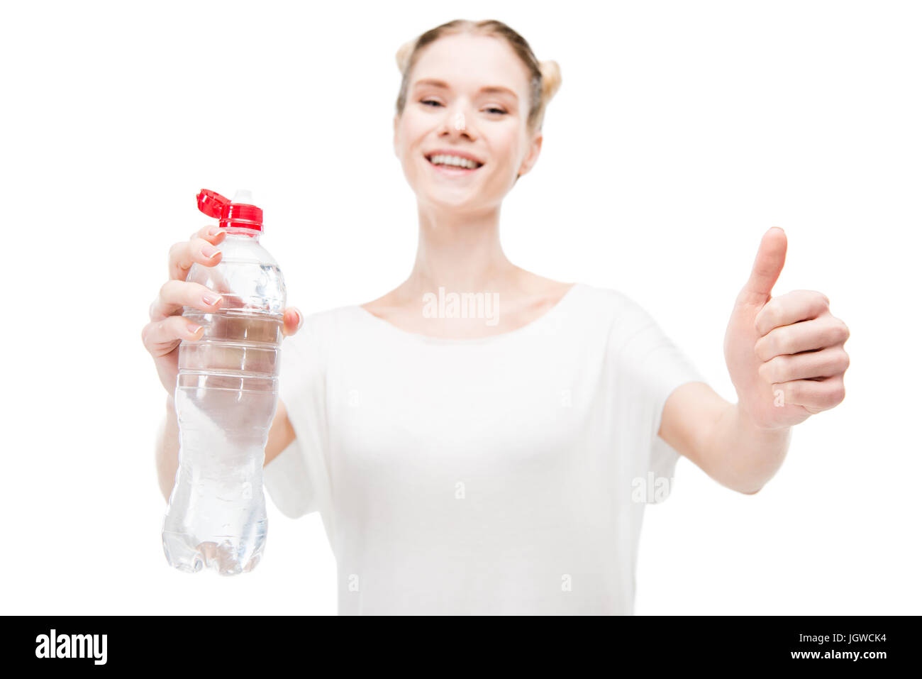 Smiling girl holding bottle with water and showing thumb up isolated on white Stock Photo