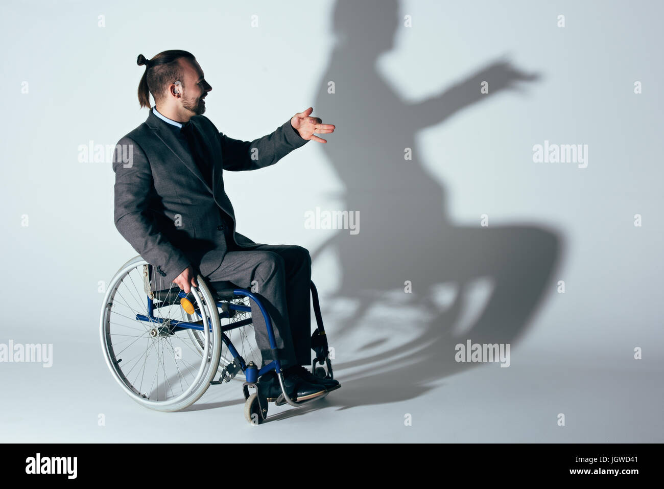 smiling man in suit sitting in wheelchair making shadow of dog on white wall Stock Photo