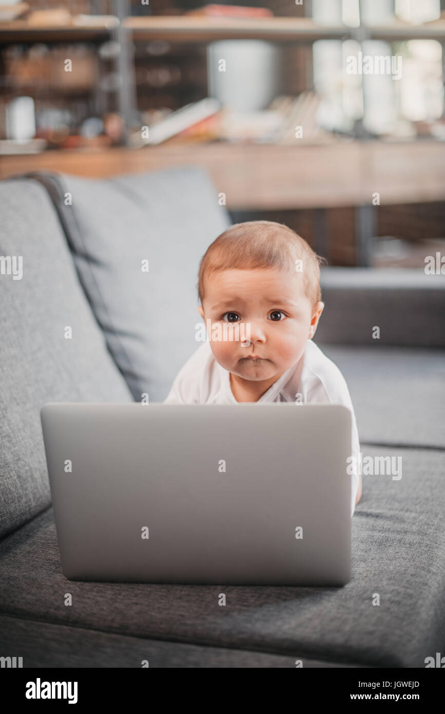 Portrait of cute baby boy using laptop on the couch at home Stock Photo ...