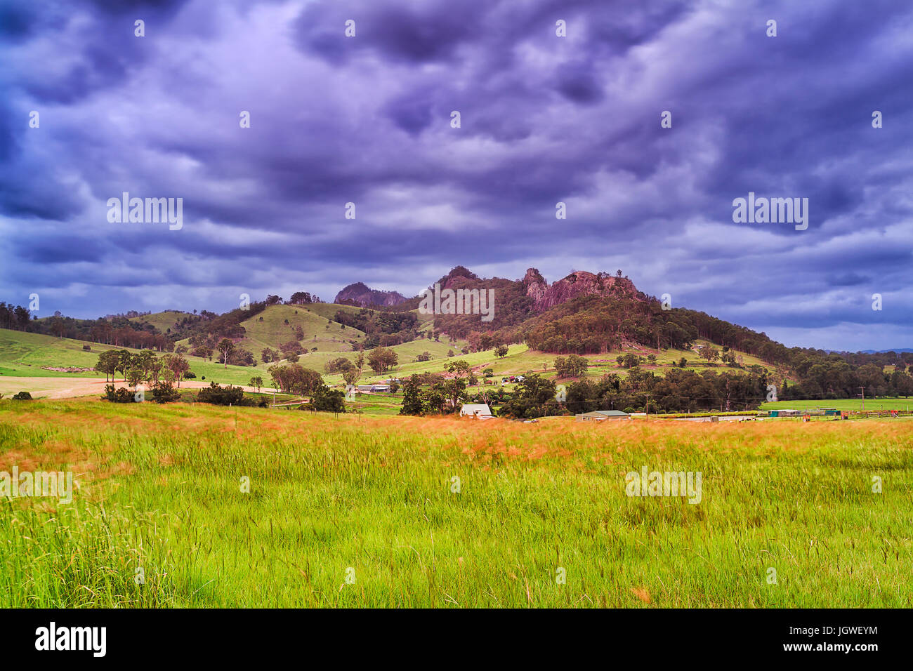 Remote agricultural farm in the middle of green pasture filed under Gloucester tops rocky mountains at sunset in Australia. Stock Photo