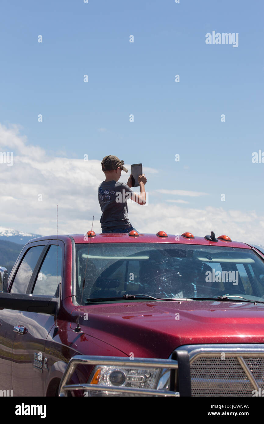 A kid (boy) is taking pictures with a tablet from the open roof of a red Dodge RAM 3500 truck in Grand Teton National Park, Wyoming, USA Stock Photo
