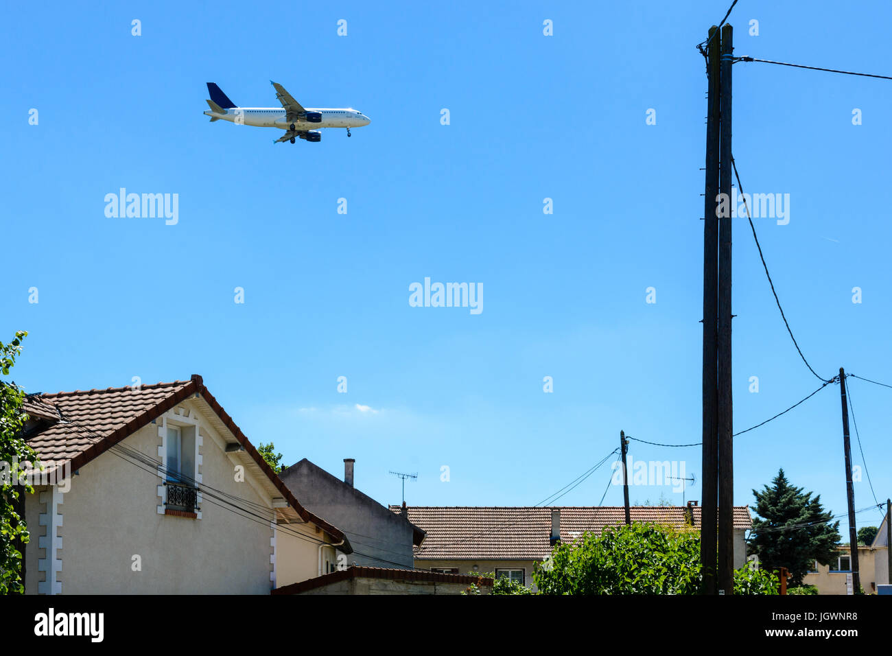 An airliner in landing approach flying above a residential area with houses in the foreground. Stock Photo