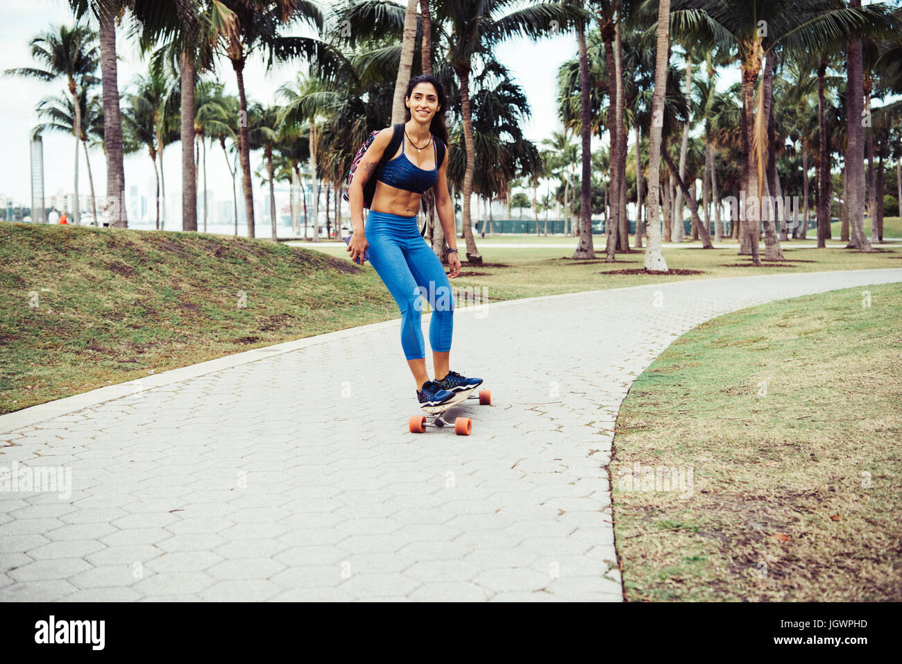 Young woman skateboarding through park, smiling, South Point Park, Miami Beach, Florida, USA Stock Photo