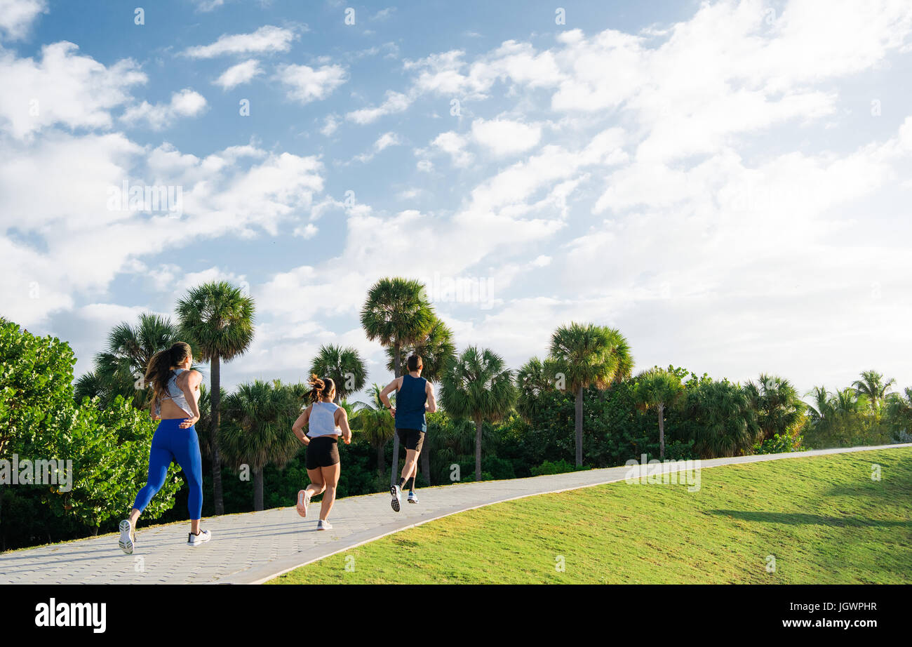 Three friends, running together outdoors, rear view, South Point Park, Miami Beach, Florida, USA Stock Photo