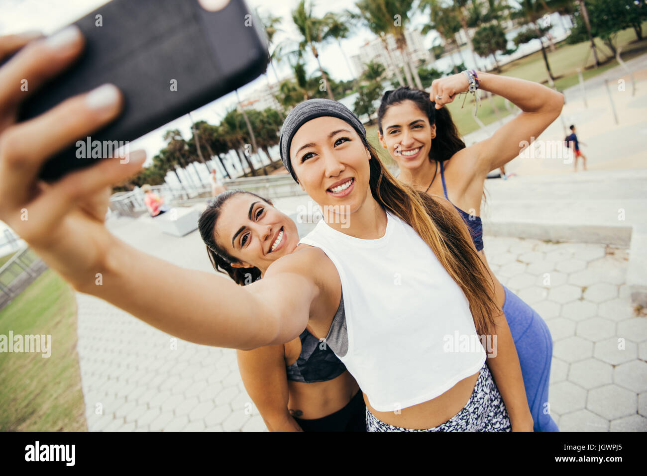 Three female friends, wearing sports clothing, taking selfie using smartphone, South Point Park, Miami Beach, Florida, USA Stock Photo