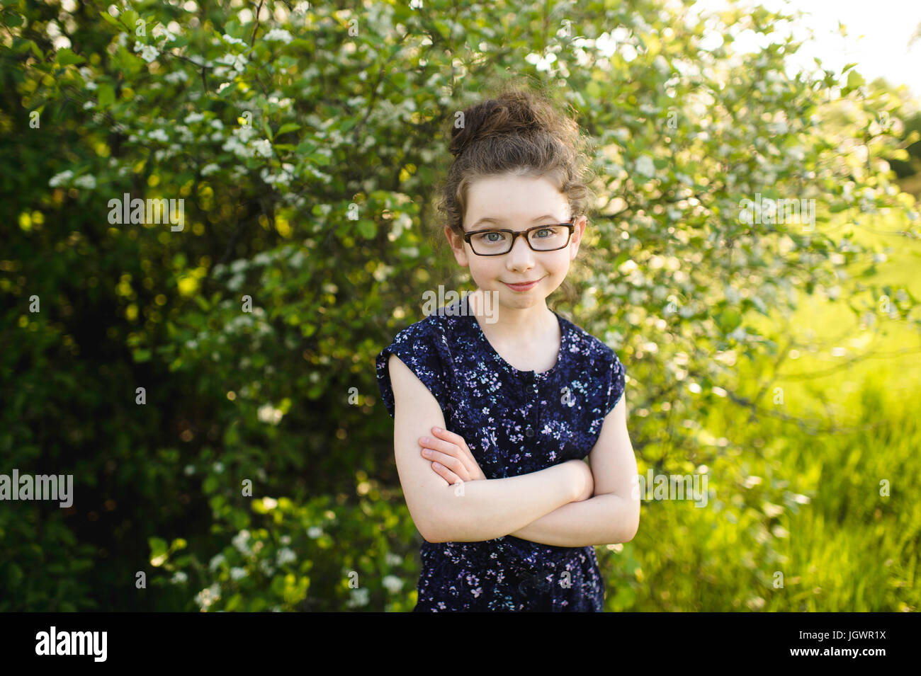 Portrait of girl wearing eye glasses in field with blossoming trees Stock Photo