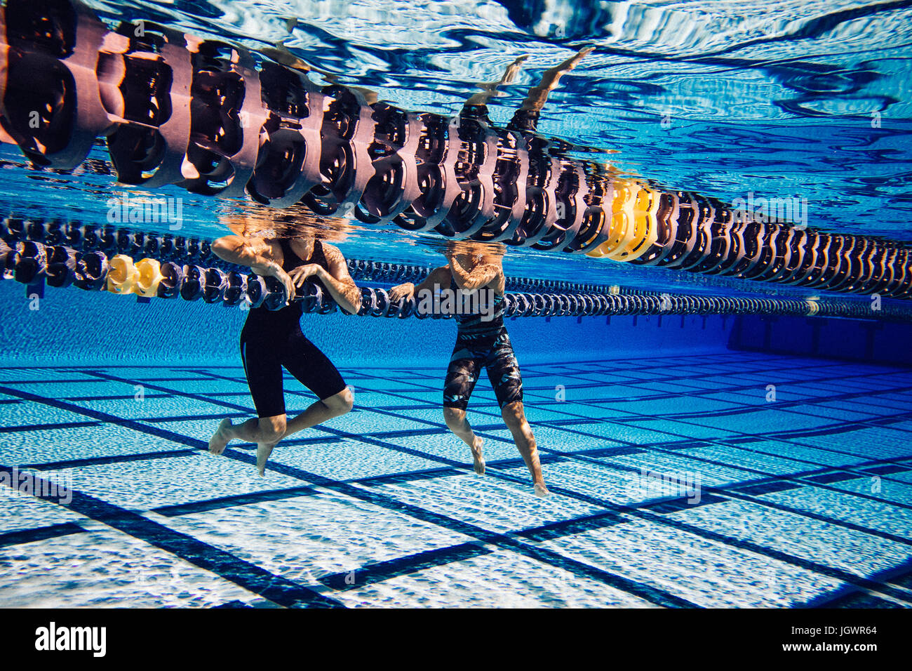 Swimmer resting on lane divider in pool talking to friend Stock Photo