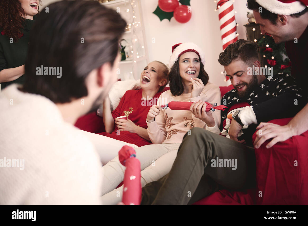 Young adult friends pulling christmas crackers on sofa at christmas party Stock Photo