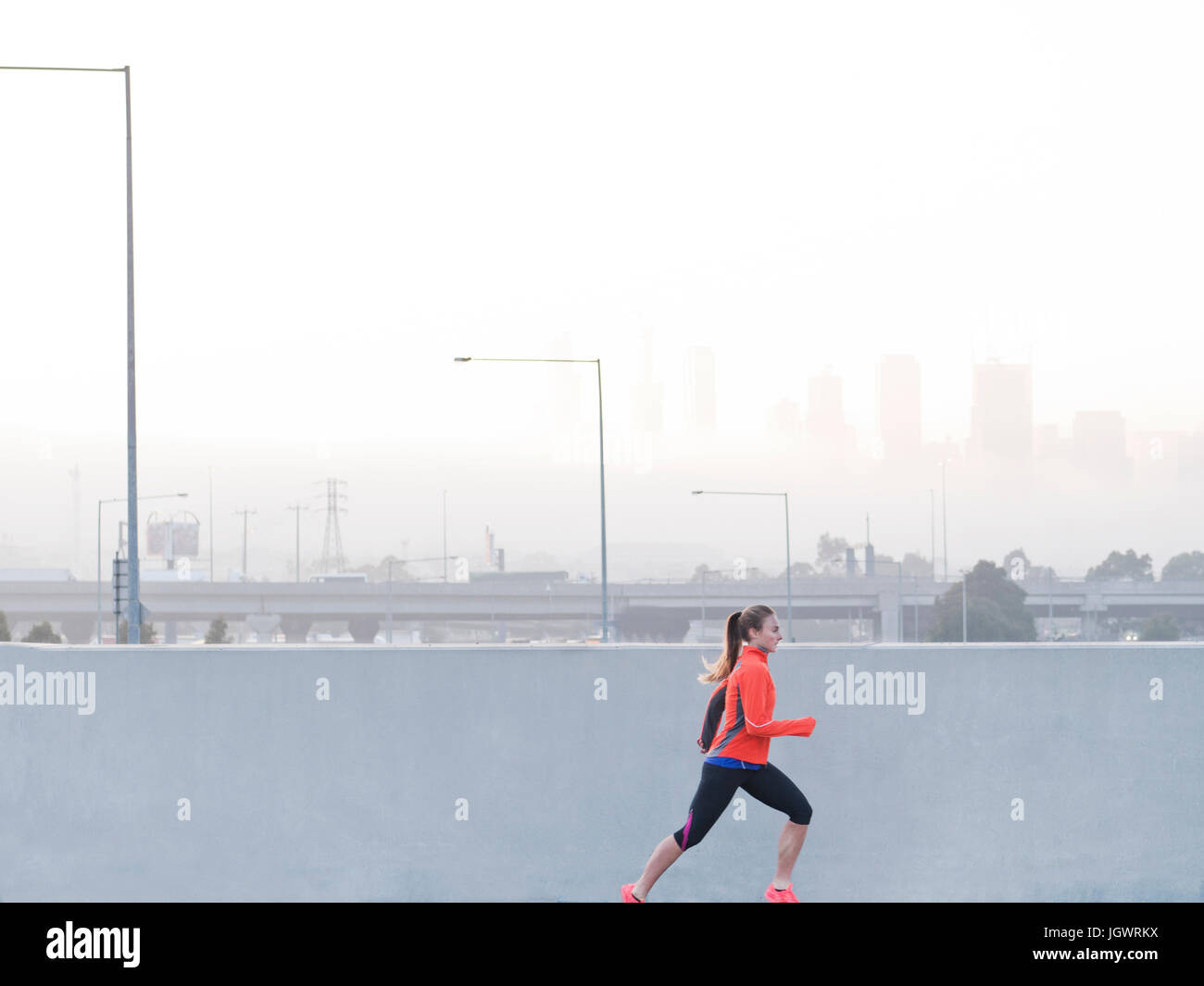 Female runner running in misty morning cityscape, Melbourne, Australia Stock Photo