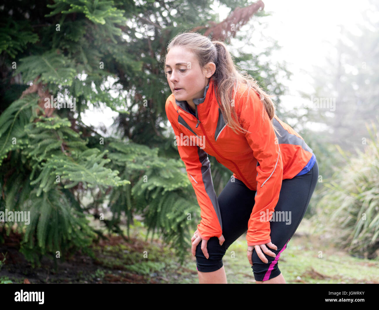 Exhausted female runner bending forward with hands on knees in park Stock Photo