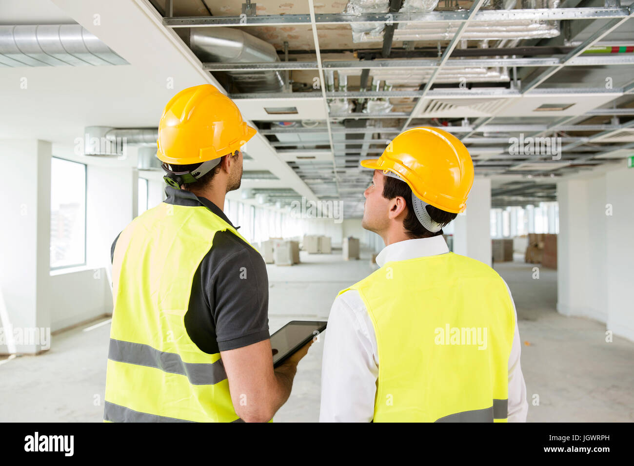 Two men wearing hi vis vest, having discussion in newly constructed office space, rear view Stock Photo