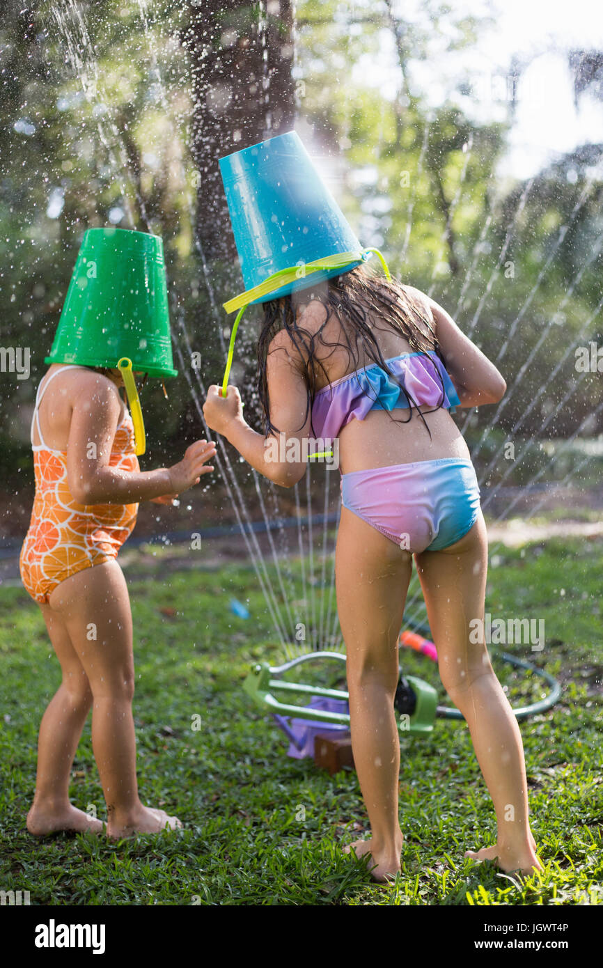 Girls with buckets on head playing with garden sprinkler Stock Photo - Alamy