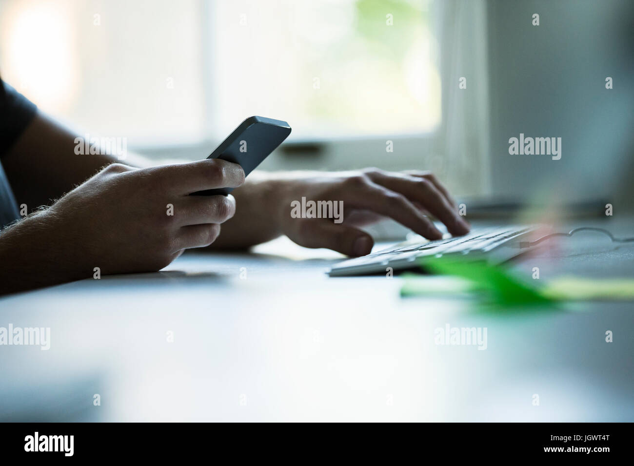 Hand of male designer using smartphone and typing on keyboard at creative studio  desk Stock Photo