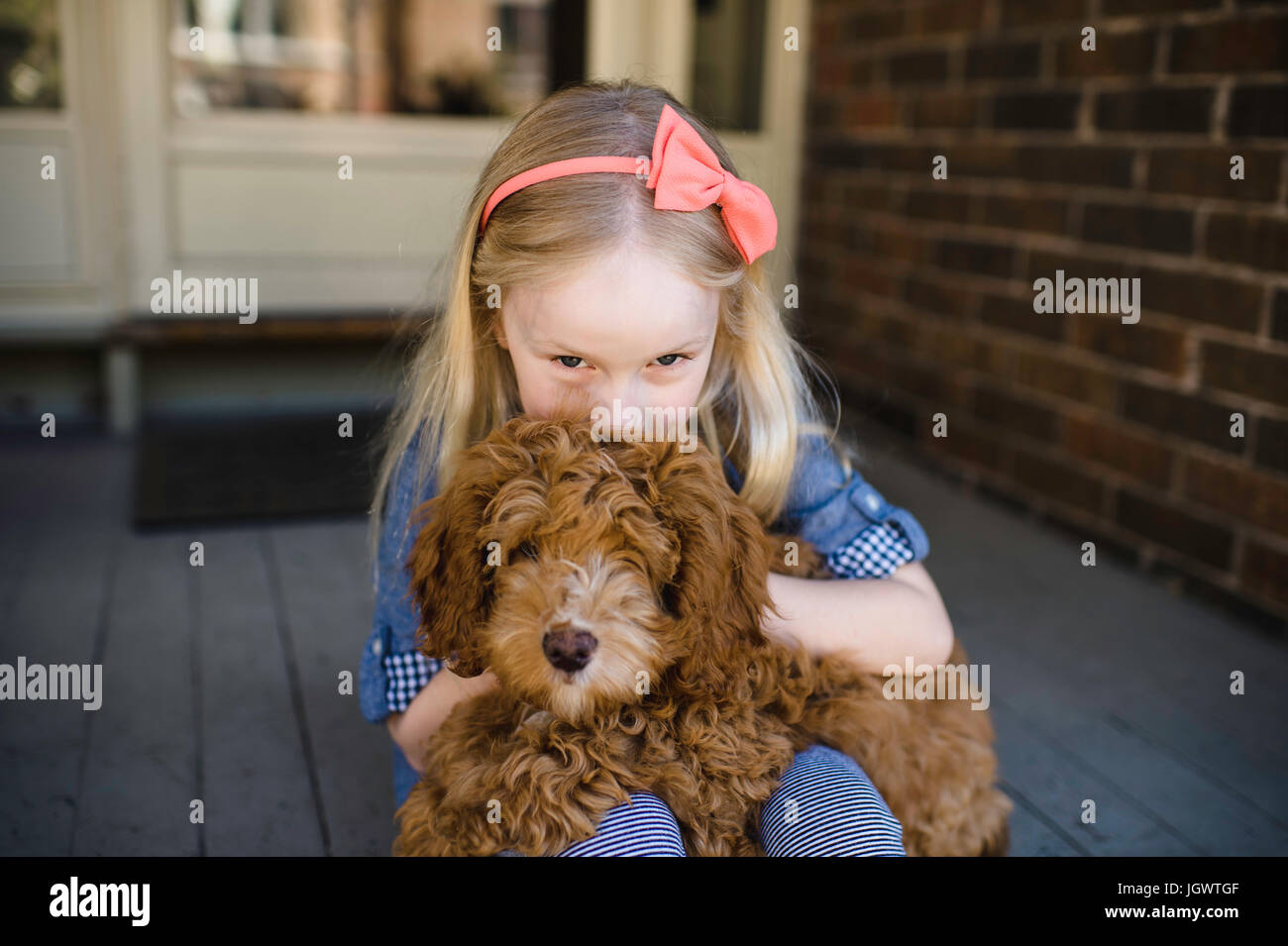 Portrait of girl kissing red haired puppy on front porch Stock Photo