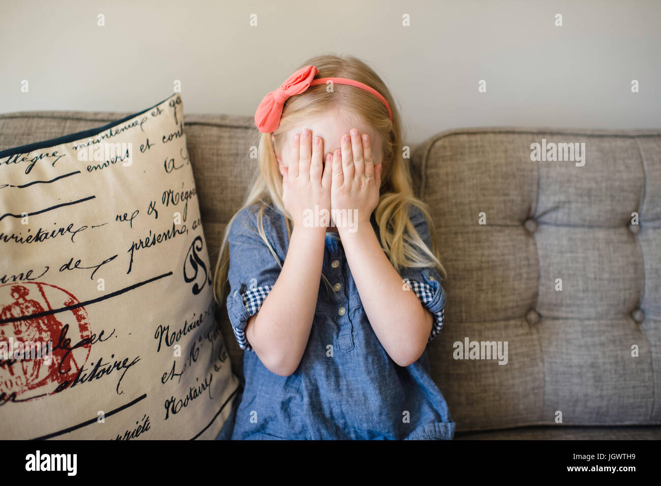 Girl on sofa covering her face with hands Stock Photo