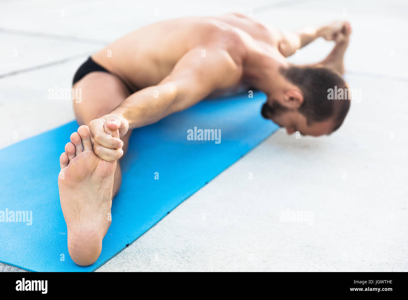 Man practicing yoga, sitting on yoga mat doing the splits and touching toes Stock Photo