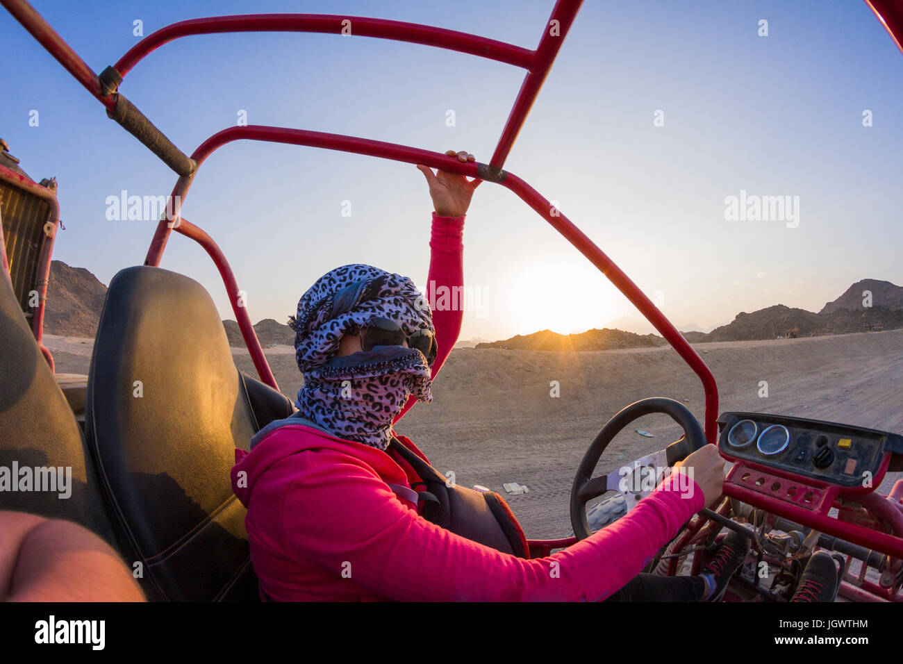 Young woman with head wrapped in scarf driving beach buggy in desert, Hurghada, Al Bahr al Ahmar, Egypt Stock Photo
