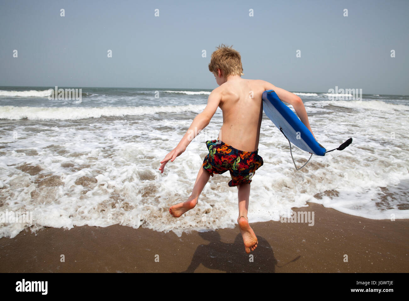Rear view of boy with bodyboard jumping in sea, Goa, India, Asia Stock Photo