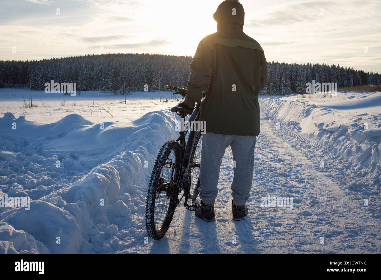 Rear view of male mountain biker watching sunset over snow covered landscape Stock Photo