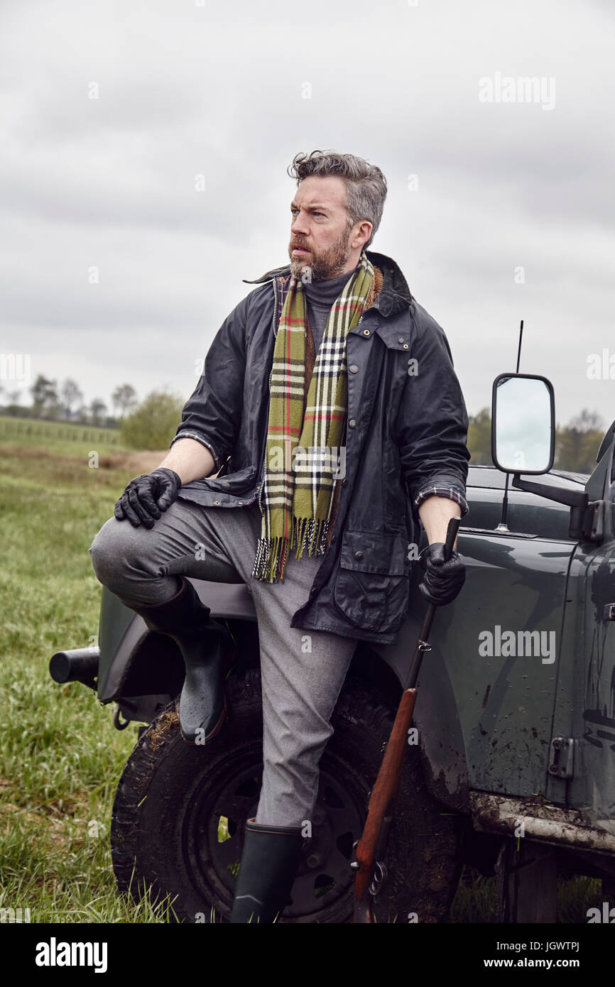 Man hunting, leaning against off road vehicle in field with shot gun Stock Photo