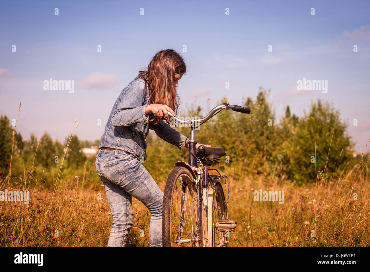 Teenage girl leaning mounting her bicycle in field Stock Photo