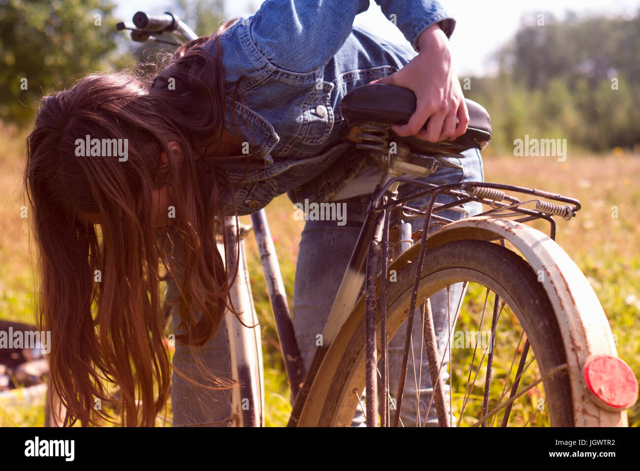 Teenage girl leaning over her bicycle in field Stock Photo